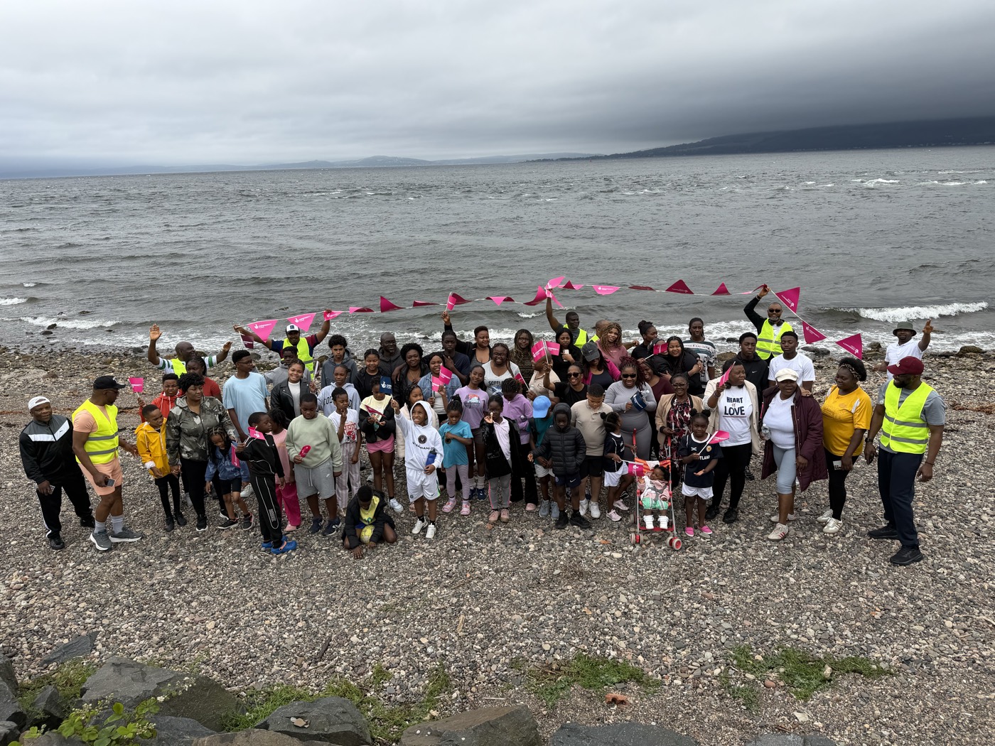 The whole group on the shingle beach at Wemyss Bay, waving pink flags beneath a grey sky